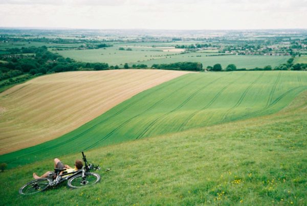 paysage d'un grand champ vert avec au milieu un homme qui se prélasse à côté de son vélo VTT